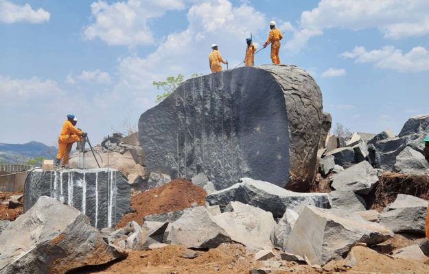 Arbeiter in orangenen Anzügen au einem großen Granitstein